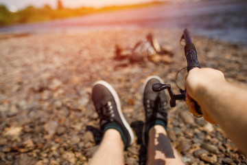 Man holds fishing rod from first person, river in background.