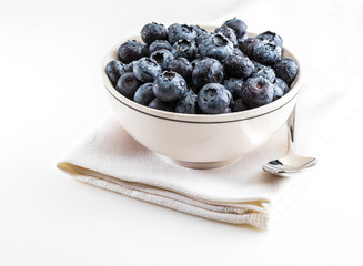 Fresh and raw blueberries in delicate white porcelain bowl. Isolated and on white background.