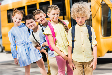 group of adorable pupils looking at camera while standing in row in front of school bus