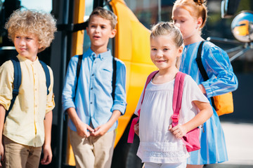 Obraz premium adorable pupils standing near school bus and looking away