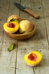 Naklejka na ściany i meble Three ripe velvet peaches in a wooden bowl on a wooden background. Rustic style.