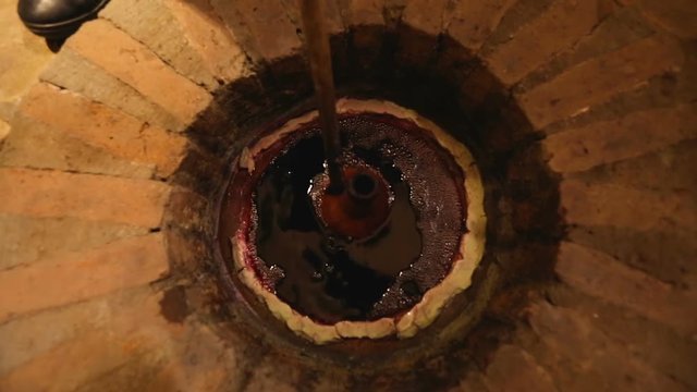 Person taking wine from qvevri buried underground, Georgia winemaking traditions