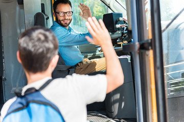 handsome smiling bus driver greeting schoolboy who entering bus