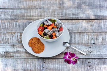 Colorful exotic fruit salad in in the white bowl on rustic wooden background.
