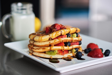 Pancakes with fresh berries, mint and maple syrup on white plate closeup