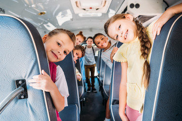 group of cute schoolchildren riding on school bus and looking at camera