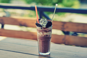 Iced coffee with whipped cream and caramel ice cream in tall glass on rustic wooden table, selective focus. Cookies and  coffee in the coffee shop with blur outdoor background, selective focus..