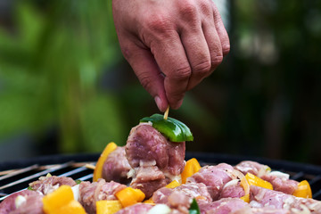 Man's hand holding a skewer with raw meat for barbecue..