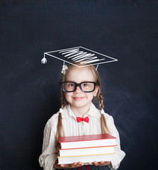 Portrait of cute schoolgirl with graduation hat and books in classroom. Back to school