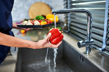 Woman washing red pepper in kitchen.