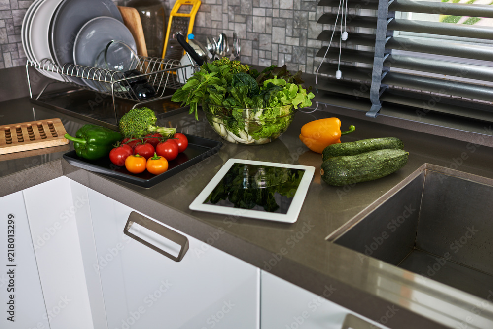 Wall mural Cooking concept, fresh kitchen herbs, vegetables  and tablet computer on kitchen  table.