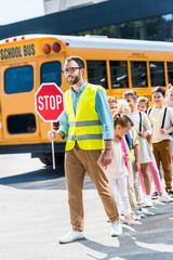 traffic guard crossing road with happy pupils in front of school bus