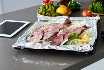 Raw ingredients. Fish and vegetables - broccoli, onions, peppers, lime and spices on the kitchen table. Cooking baked fish with vegetables.