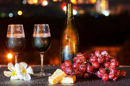 Two Glasses Of Red Wine, Cheese And Grapes On The City At Night Background.