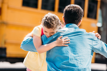 rear view of father and daughter embracing in front of school bus