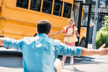 father with open arms waiting for daughter while she running from school bus