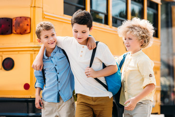 Fototapeta premium happy little schoolboys having fun together in front of school bus