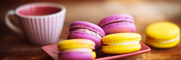 A cup of hot black coffee and bright macaroons on a wooden table at dark background with colorful bokeh