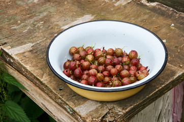 Ripe red gooseberry in a bowl on a wooden table