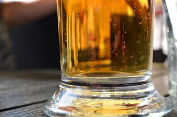 Close up of full glass of golden beer standing on wooden table in outdoor pub. Summer vacation begins. Concept of drinking problems and alcohol addiction