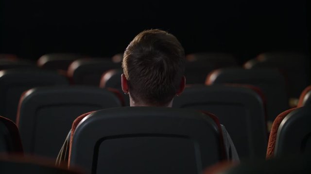 Stylish guy sitting in empty movie theater alone. Back view of man head in cinema. Lonely guy sitting in empty room after movie. Young man sitting alone in empty cinema