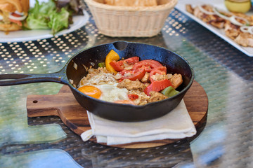 Fried eggs in a frying pan with vegetables and bread for breakfast on a gray background.