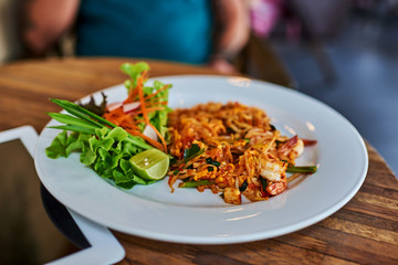 Thai stir-fried rice noodles on wooden table with blurred man.  lunch break.