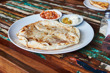 Mexican quesadilla wrap with chicken, corn, sweet pepper, salsa and guacamole on a plate.