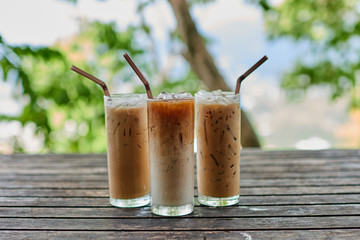 Three tall glasses of iced coffee on old wooden table.