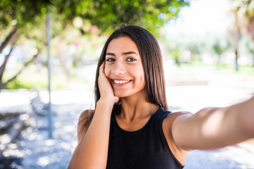 Portrait of pretty young latin girl taking selfies with her smart phone in the street