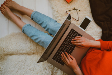 Top view of a young woman holding laptop computer on her lap while sitting at home. Woman using laptop for browsing internet store. Online shopping concept. Young woman sitting on carpet at home