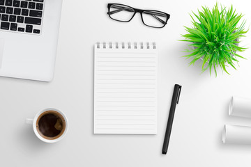 Empty notepad surrounded with office supplies. Laptop computer, cup of coffee, plant, glasses and...