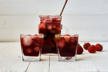 Refreshing sangria or punch with fruits in glasses and pitcher.  Traditional summer drink beverage. Red wine, strawberries, oranges, lemon, and green apple. On a wooden rustic table with copy space..