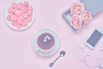 Workspace with  smartphone, a cup of hot  herbal tea, flowers and a marshmallow  on pink table. Woman work desk for creativity. Still life of pink items  with pastel accents. Top view.