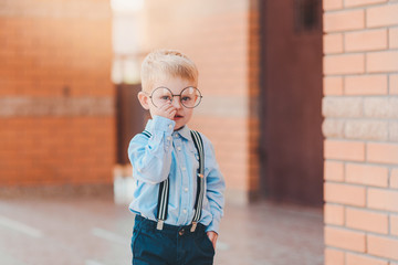 Back to school. Happy little boy in glasses with backpack and books against brick wall of the school building.