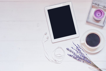 Workspace with cup of black coffee,  digital tablet with empty screen, candle, fresh cookie and flowers on white vintage background. Wireless communication concept. Top view, flat lay, copy space.