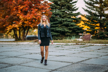sexy woman in black short dress and leather jacket walks through the Park outdoors