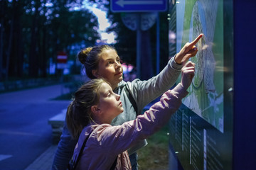 Two girls teenager are looking for the way route on the map scheme at night dark