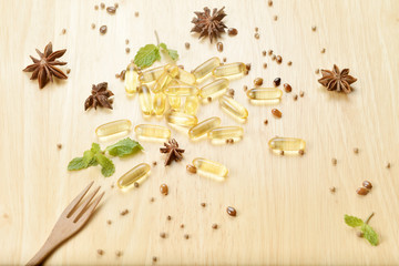 Fototapeta na wymiar Medicine herb, Cod liver oil omega 3 gel capsules with healthy medicinal plant on wooden brown tone background with a wooden fork on foreground.