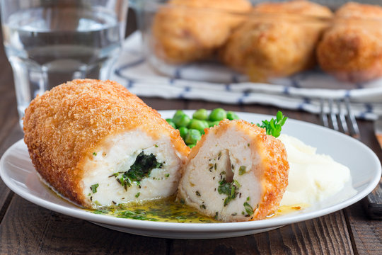Chicken Kiev, ukrainian cuisine. Cutted chicken cutlet in bread crumbs stuffed with butter and herbs, served with mashed potato and green peas, on brown background, horizontal