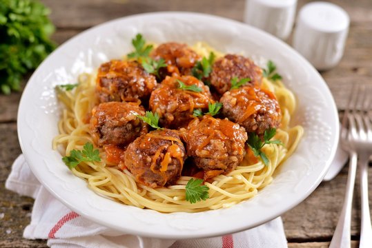 Meatballs with rice, onions, carrots with spaghetti in tomato sauce. Rustic style, rustic food on an old wooden background.