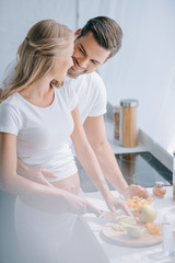 Obraz na płótnie Canvas happy pregnant woman and husband cooking fruits salad together in kitchen at home