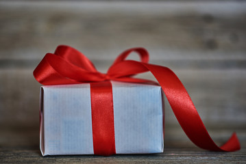 White gift box wrapped with red ribbon and bow on the  vintage wooden wall background with copy space. Presents for Christmas, Valentine, birthday or Mother's Day greeting. Holiday packing concept.