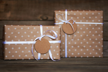 Two gift boxes wrapped in recycled paper with white ribbon bows and tags on old wooden background. Parcels or gifts. Background for your design. Vintage style. Holiday packing concept..