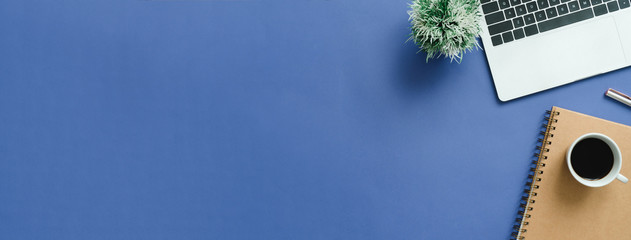 Minimaler Arbeitsplatz - Kreatives Flachfoto des Arbeitsplatzschreibtisches. Schreibtisch von oben mit Laptop, Notebooks und Kaffeetasse auf blauem Hintergrund. Panorama-Banner-Hintergrund mit Kopienraum.