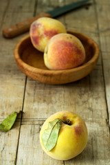 Three ripe velvet peaches in a wooden bowl on a wooden background. Rustic style.