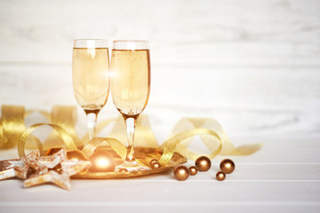 Christmas holiday background. Celebration theme. Two glasses of champagne with gold ribbon and Christmas decor on the blurred white  background. Celebration concept, free space for text.
