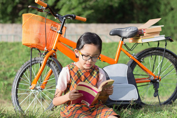 student girl with bicycle sittingon the grass reading a book in garden at summer time