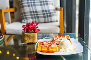 Waffles with fresh ripe red strawberries and icecream served on a plate on table in the room of restaurant