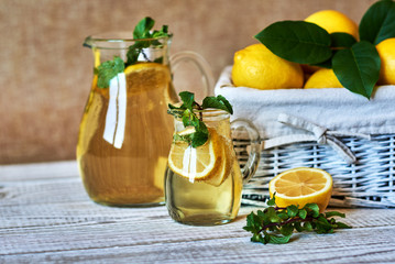 Fresh lemons in a white basket with  leaves and homemade lemonade in a jug and glass with lemon slices and mint.